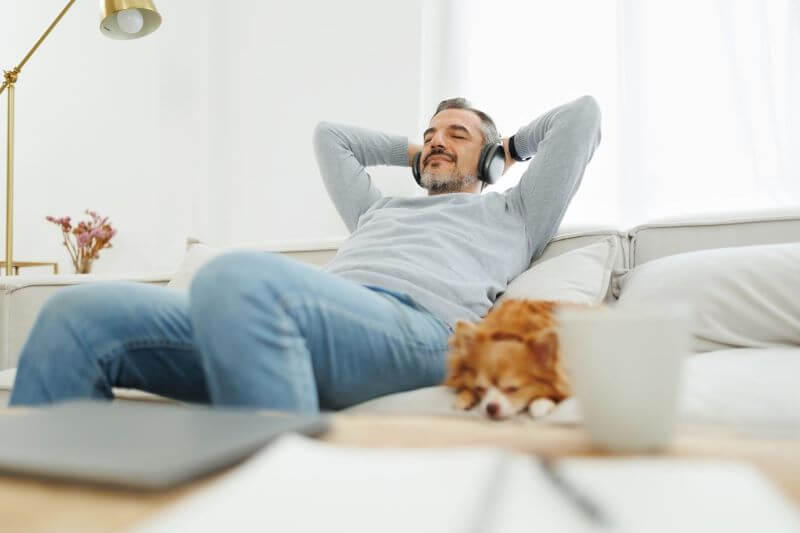 Happy Mature Adult man sitting on sofa relaxing with dog