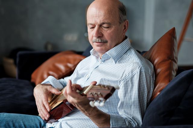 Senior hispanic man at home learning to play guitar.